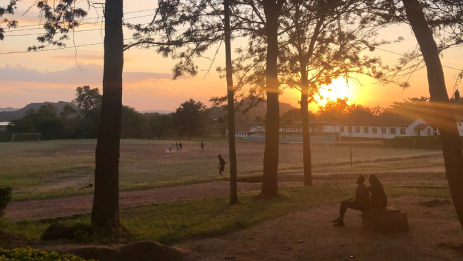 Auringonlasku Tansaniassa. Ihmisiä istumassa penkillä etualalla.